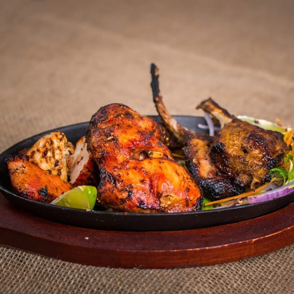Indian grilled chicken and lamb chops with lime and vegetables on a sizzling platter.