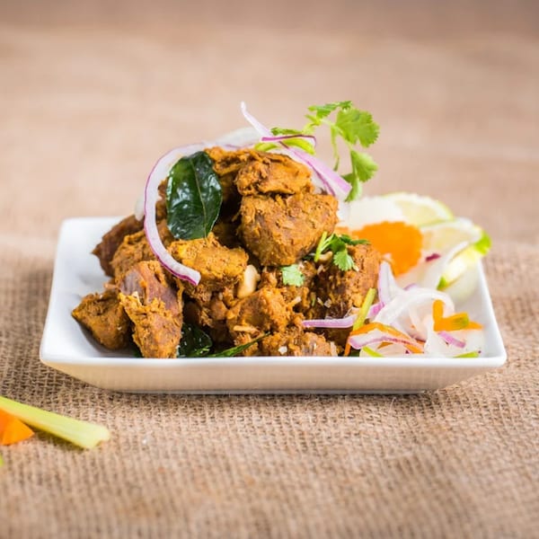 Indian chicken curry with red onions, cilantro, and lime on a white plate.