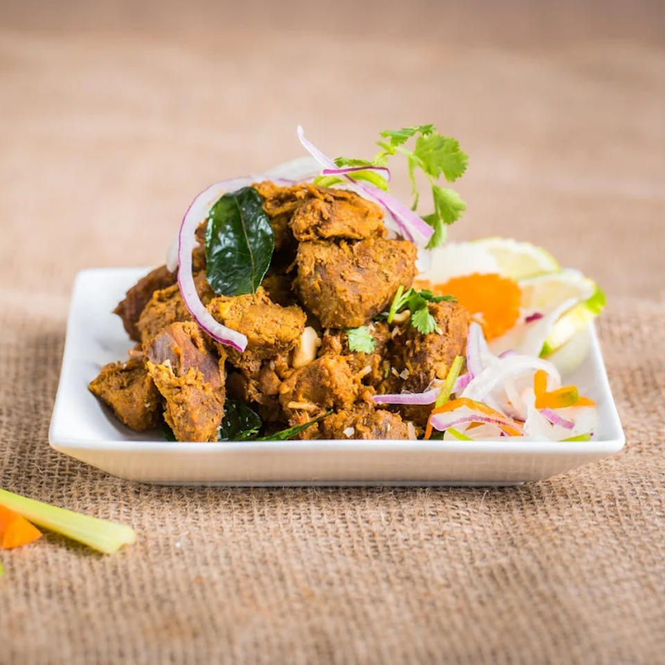 Indian chicken curry with red onions, cilantro, and lime on a white plate.