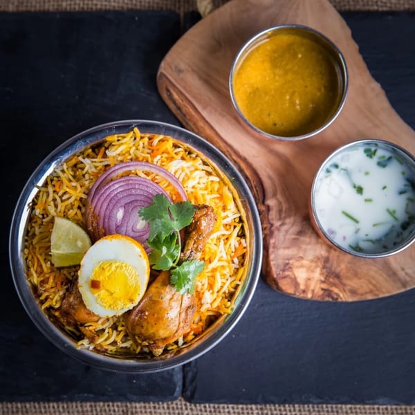 Chicken Biryani with a hard-boiled egg, red onion, lime, cilantro, and two side sauces.