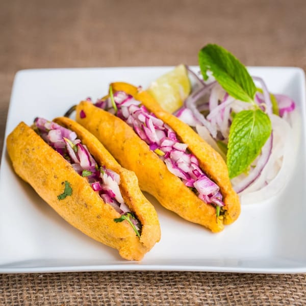 Two golden Indian chili fritters filled with red onions, served with lime and mint.