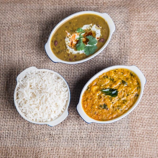 Overhead view of two bowls of Indian curry and one bowl of white rice on a burlap surface.