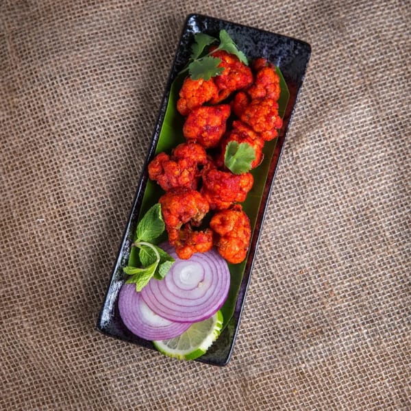 BawarcHi Indian Cuisine's bright red Gobi 65, garnished with cilantro, mint, red onion, and lime.