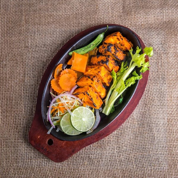 Indian chicken tikka sizzler with vegetables, lime, and chili on a dark platter.